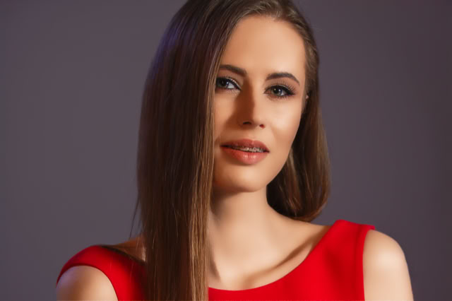 Urocze spojrzenie szatynki. Pociągła twarz. Modelka w czerwonej sukni. Zbliżenie twarzy. Kobieca sesja zdjęciowa. Portret Kobiety.