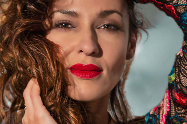 Zbliżenie twarzy naturalnej szatynki o gęstych falowanych włosch. Jej koronkowa suknia w czerwone, zielone kwiaty dodaje uroku. Kobieca sesja zdjęciowa. Portret Kobiety.