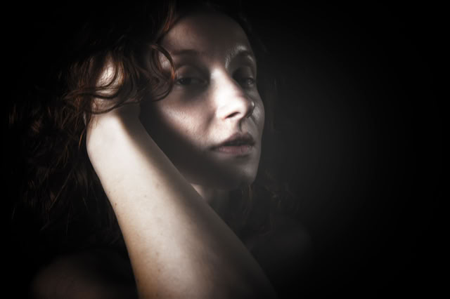 Ruda modelka wyłaniająca się z ciemności. Zblizenie twarzy pięknej kobiety. Kobieca sesja zdjęciowa. Portret Kobiety.